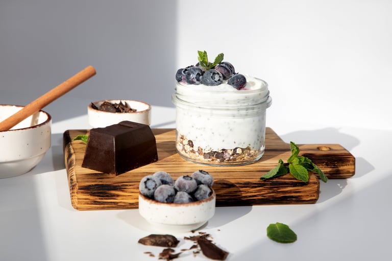 Yogurt in a glass jar with granola, chocolate, blueberries and honey on a wooden board on a white background with mint leaves