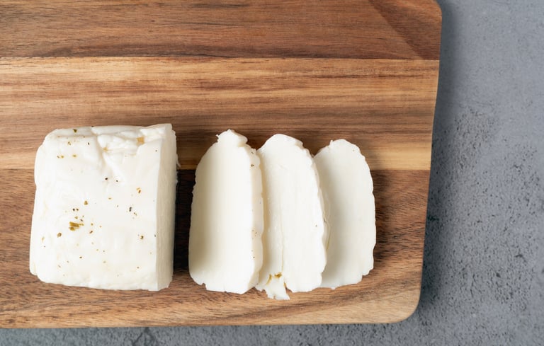 A high-angle shot showing a block and several slices of white halloumi cheese arranged on a rustic wooden board, ready for cooking