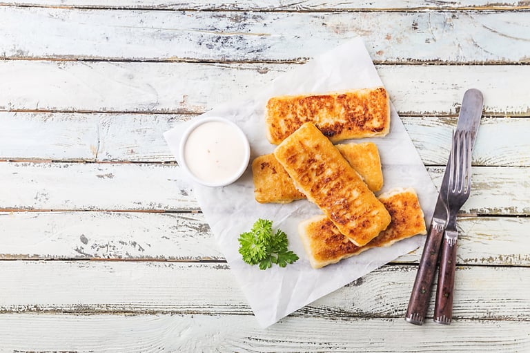 Crumbed golden fried fish fingers served with tartar sauce and salad on a white rustic wooden background, top view