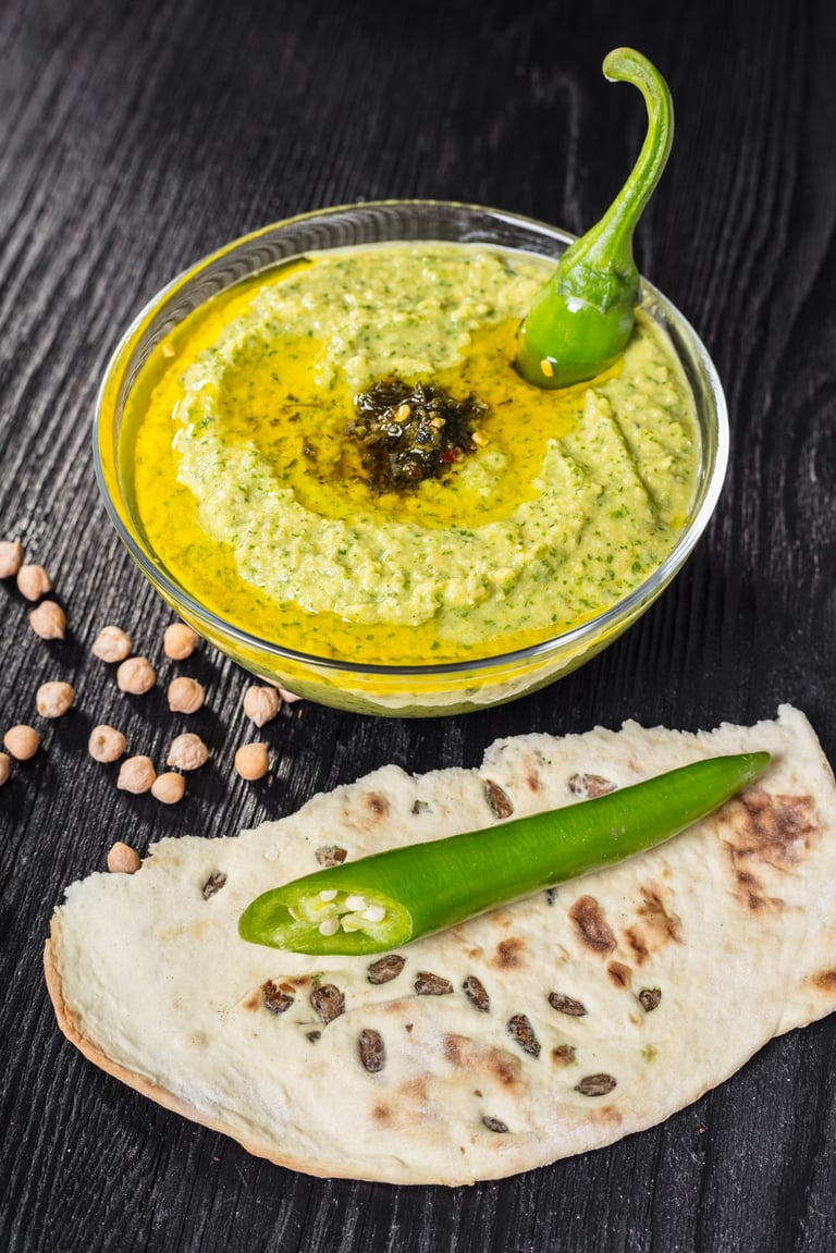 Hummus with spinach and hot pepper on a black wooden background
