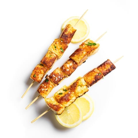 Three grilled chicken skewers on wooden sticks with lemon slices on a white background